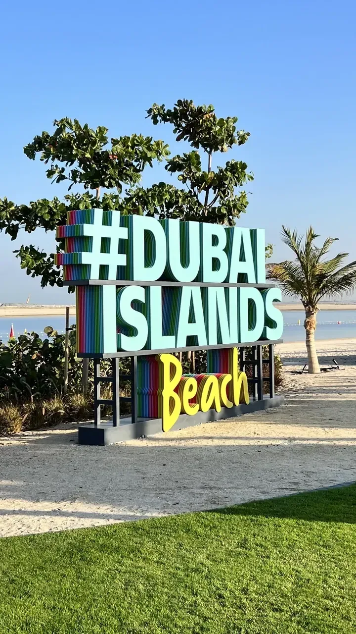 Colourful Dubai Islands Beach sign beside palm trees and the shoreline