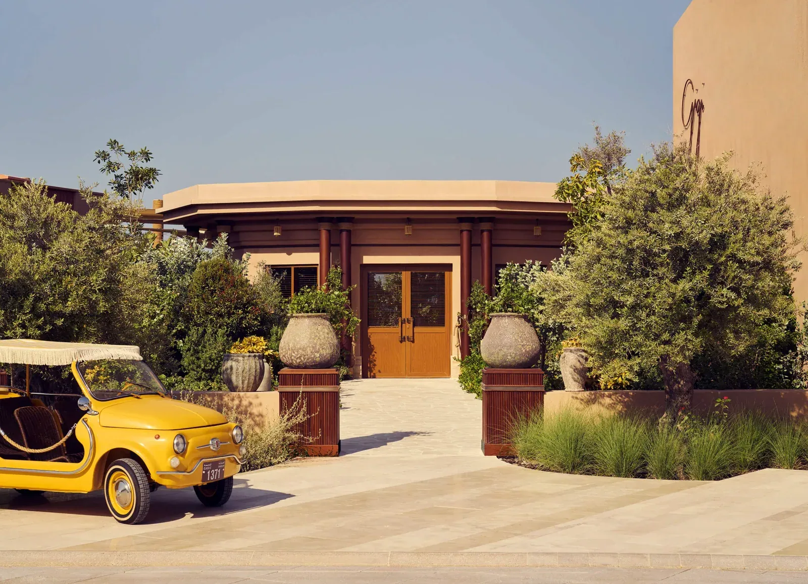 Gigi Rigolatto entrance with olive trees and a yellow vintage car at J1 Beach