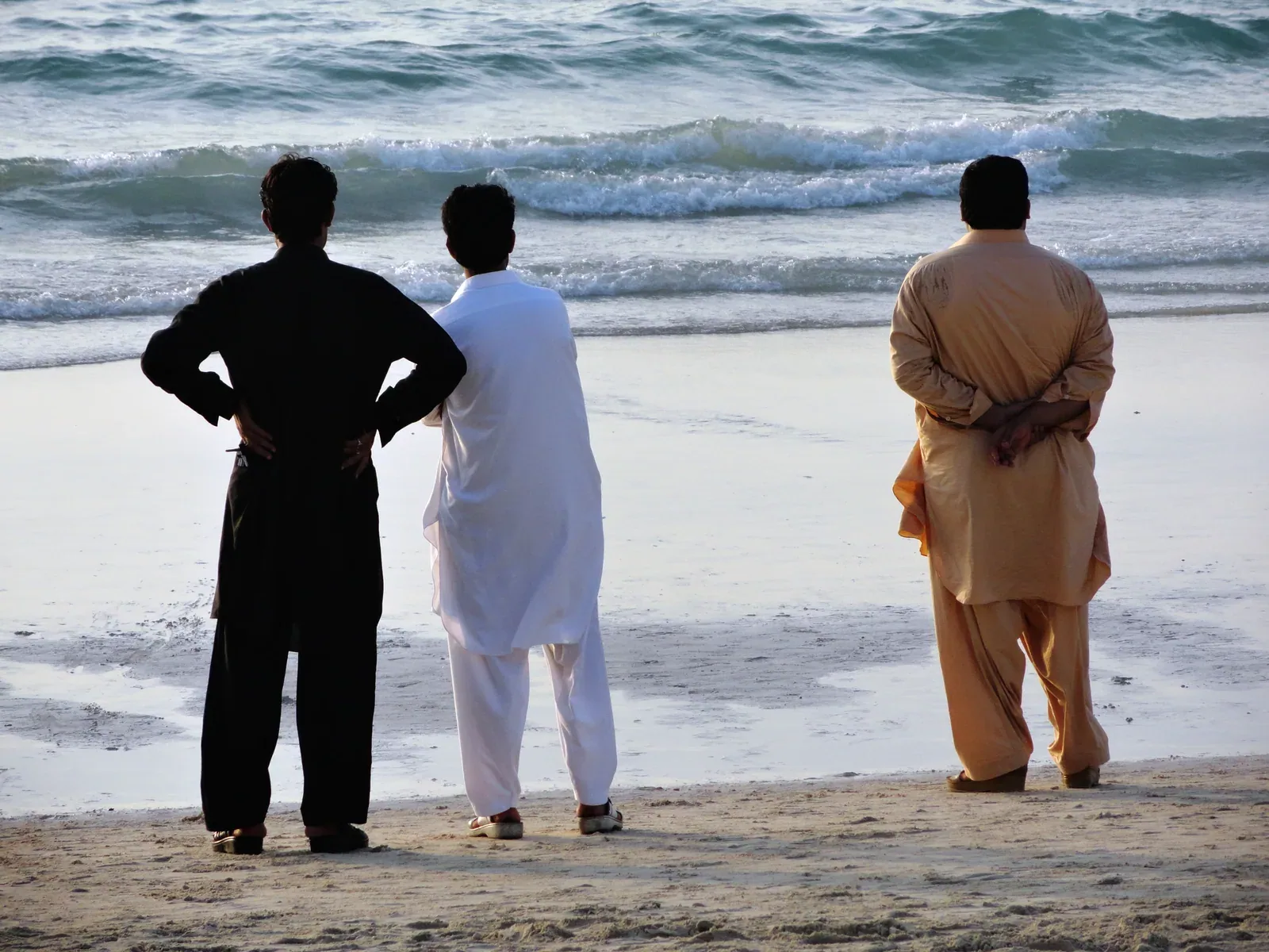 Three visitors seen from behind watching the waves at Umm Suqeim Beach