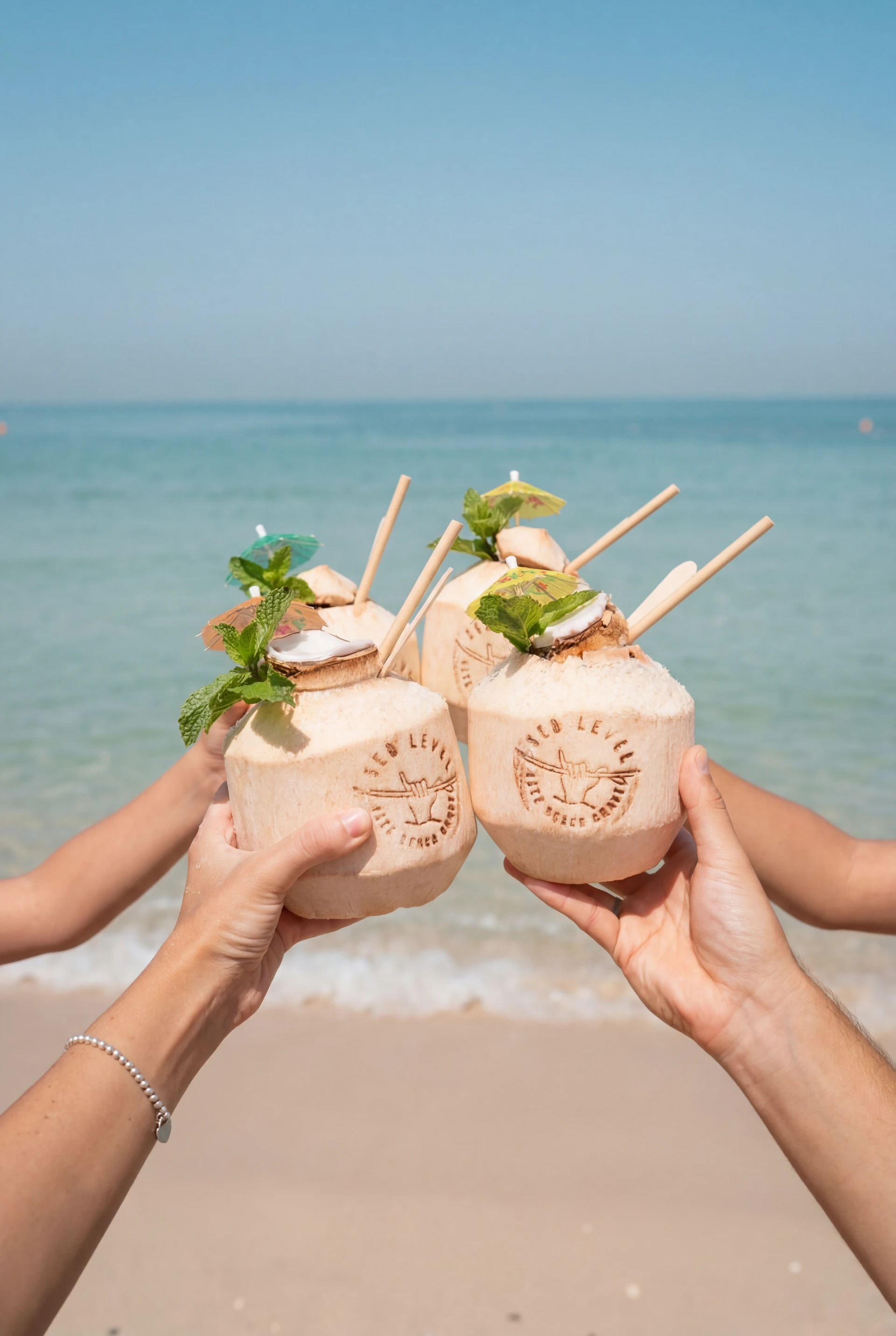 Friends raising fresh coconut drinks beside the turquoise sea
