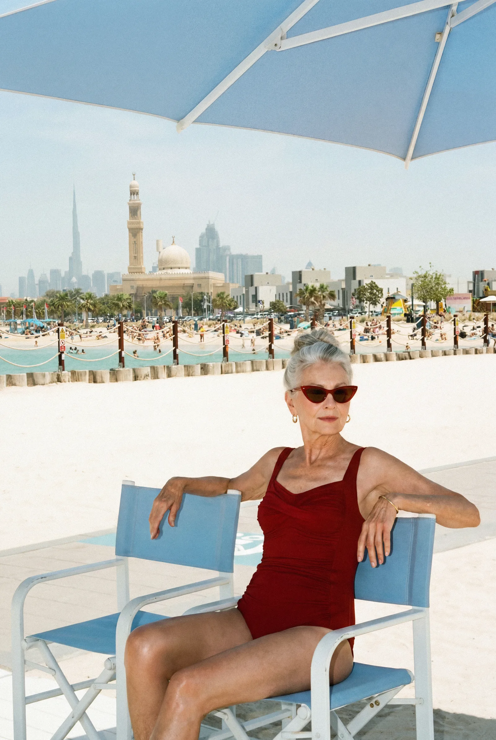 A woman in a red swimsuit relaxing beneath a blue umbrella with the Dubai skyline behind her