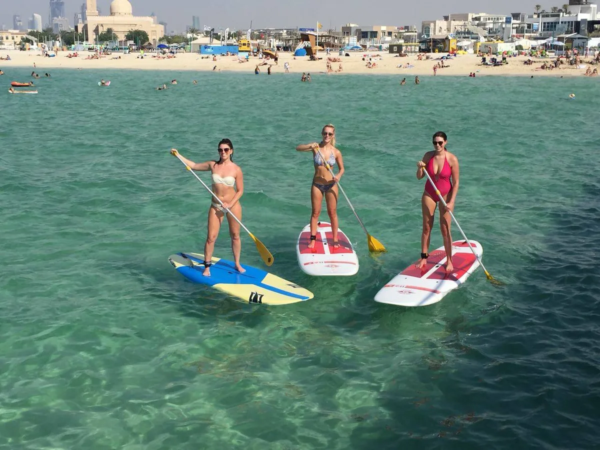 Three paddleboarders at Kite Beach with KSD’s yellow rental bus on the shore behind them