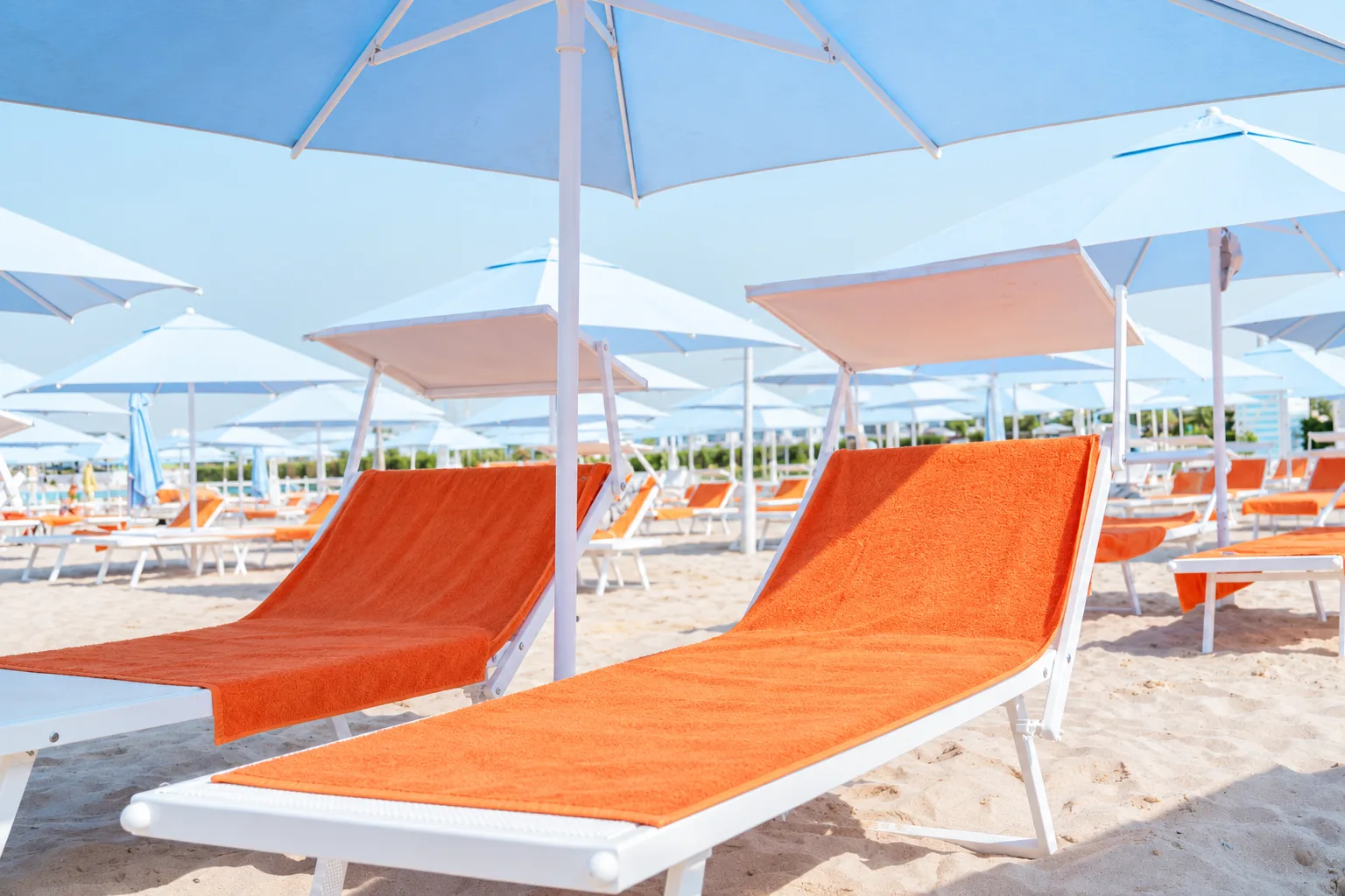 White Sole Mio sun loungers with orange towels beneath blue beach umbrellas