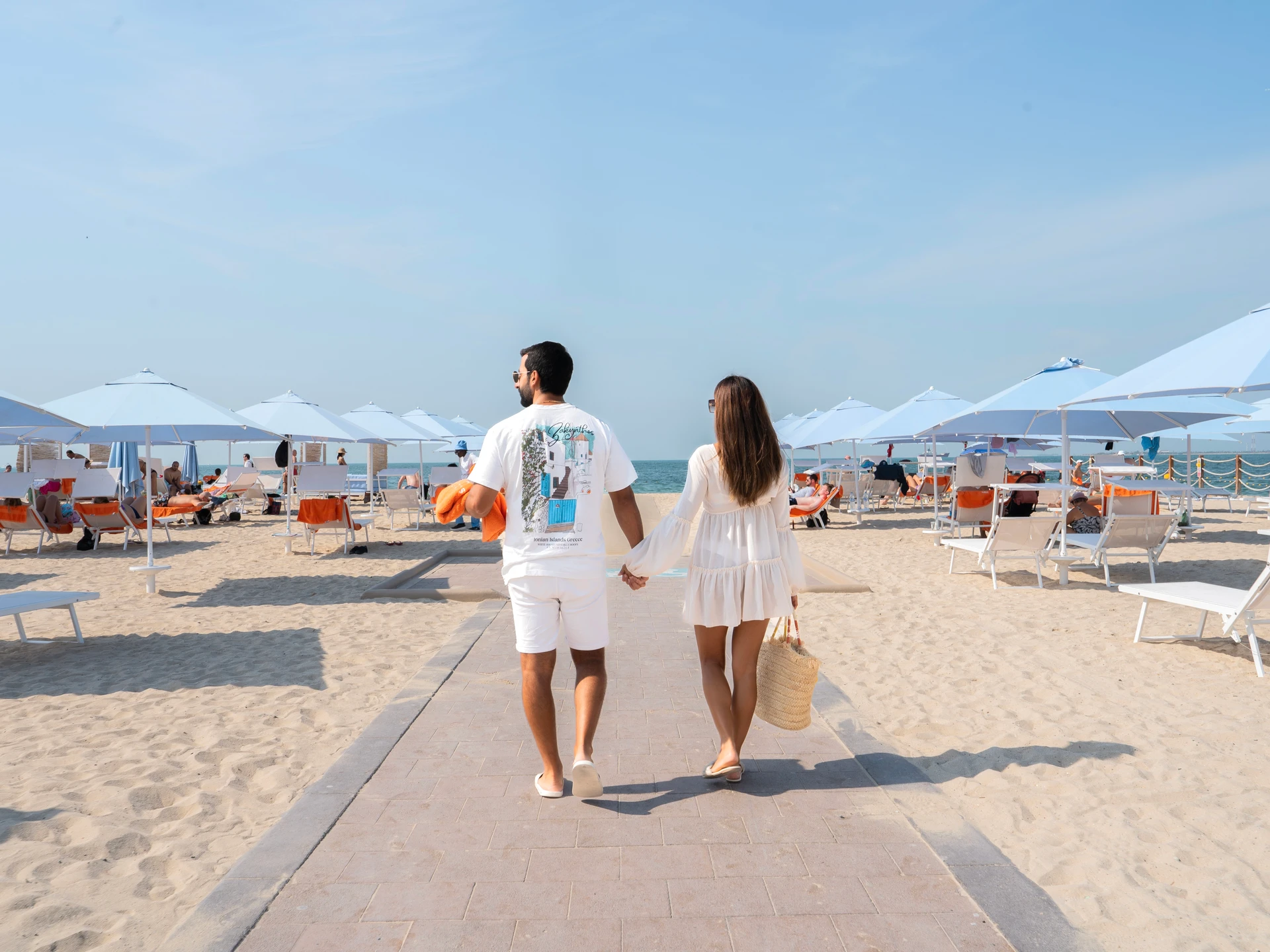 A couple walking towards the sea along the path between Sole Mio’s blue umbrellas