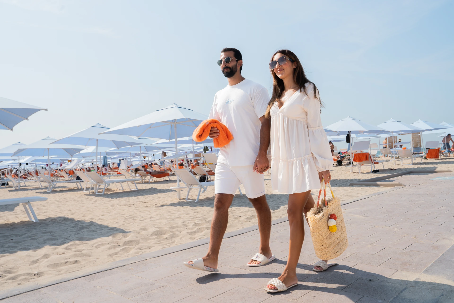 A couple enjoying a day at Sole Mio, carrying an orange towel and a beach bag