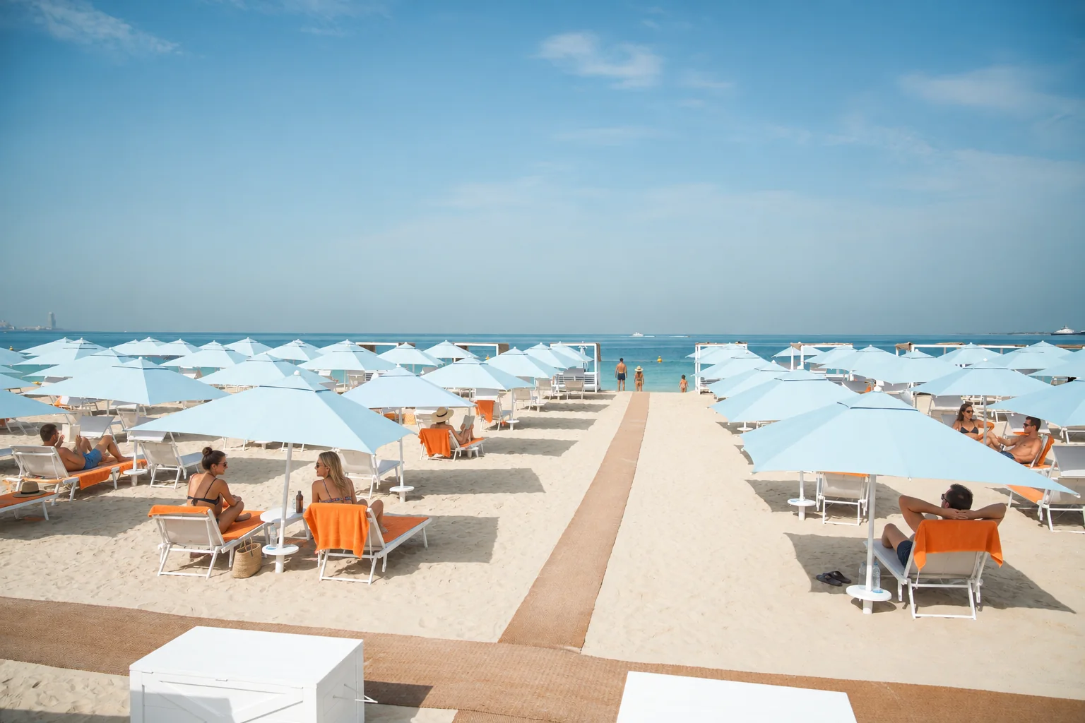 Guests chatting and relaxing on orange towels beneath blue umbrellas at Sole Mio on Kite Beach, Dubai